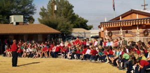 A photo of Carden of Tucson, with students sitting outside in front of the building. One of the teachers is standing on the grass speaking to the kids.